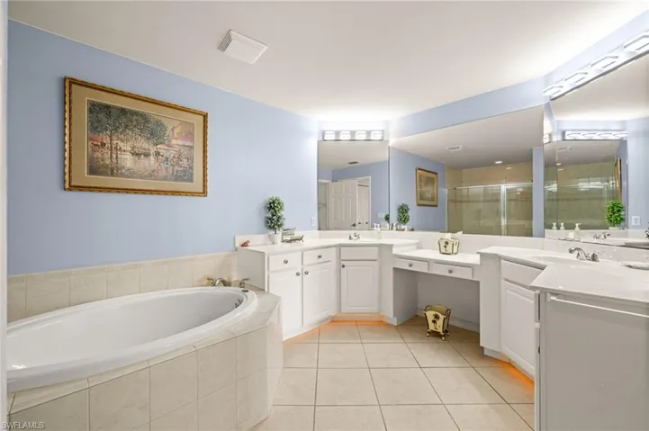 Bathroom featuring light tile patterned flooring, a stall shower, two vanities, and a bath