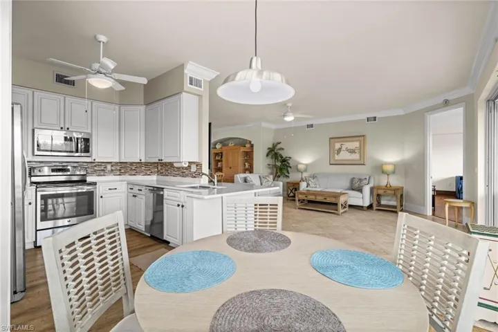 Kitchen featuring a peninsula, stainless steel appliances, white cabinetry, crown molding, and decorative light fixtures