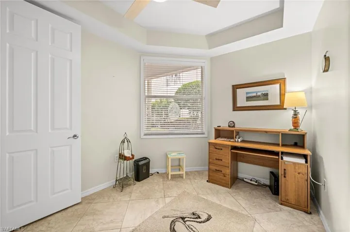 Home office featuring light tile patterned floors, a ceiling fan, and a raised ceiling