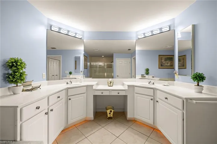 Bathroom featuring light tile patterned flooring, a stall shower, and two vanities