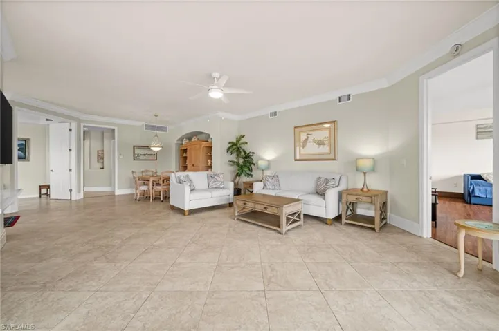 Living room featuring ornamental molding, a ceiling fan, light tile patterned floors, and arched walkways