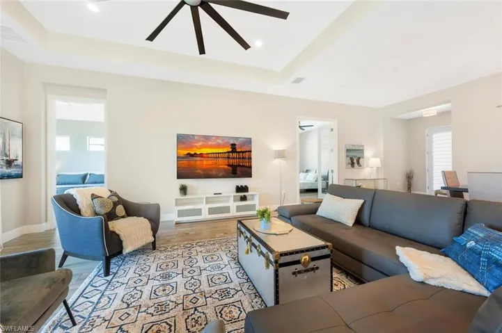 Living room featuring ceiling fan, a tray ceiling, and light wood-type flooring