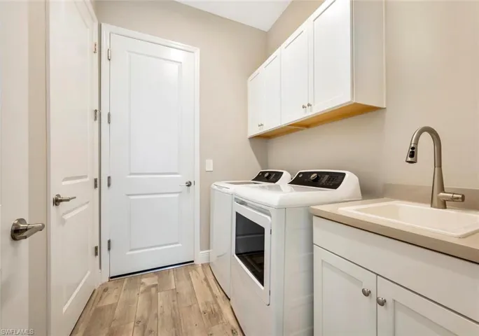 Clothes washing area featuring sink, washing machine and clothes dryer, light hardwood / wood-style flooring, and cabinets