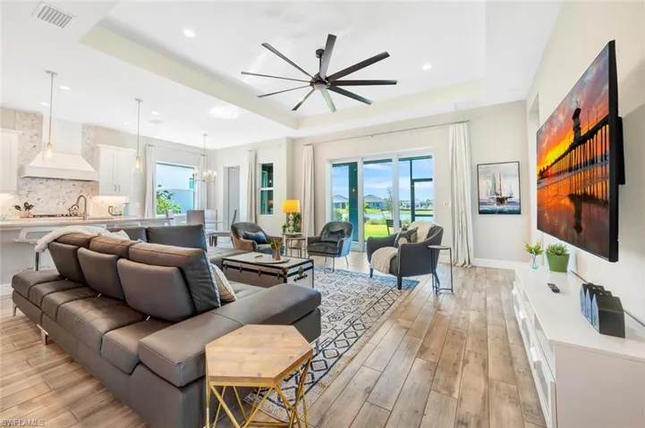 Living room with light hardwood / wood-style floors, a tray ceiling, and ceiling fan with notable chandelier