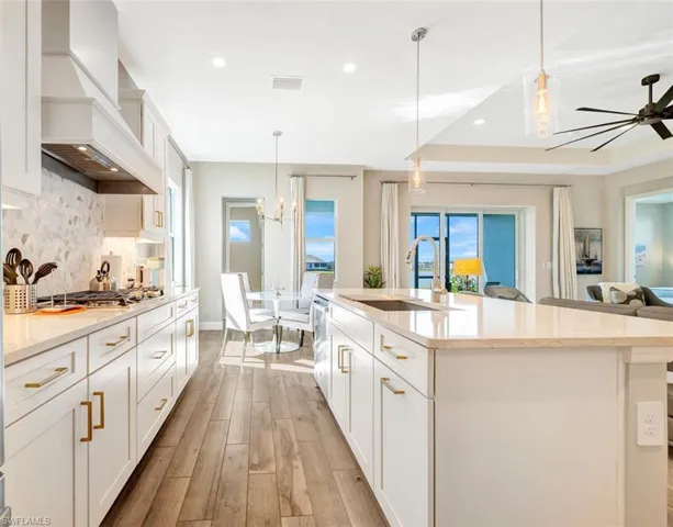 Kitchen featuring light hardwood / wood-style floors, custom range hood, a kitchen island with sink, backsplash, and sink