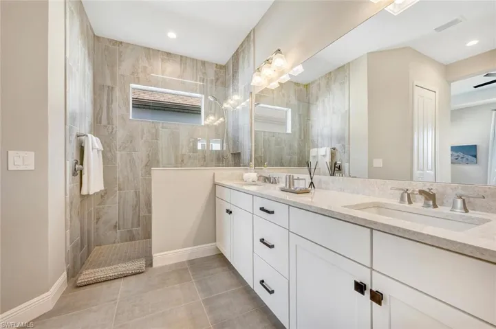 Bathroom with dual sinks, tiled shower, tile floors, a wealth of natural light, and large vanity