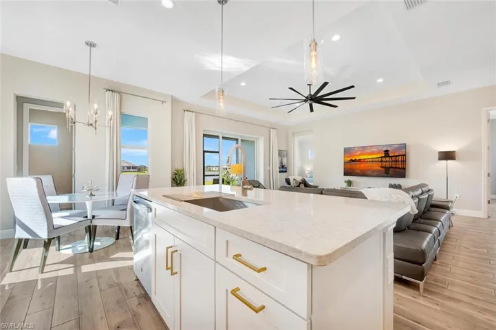 Kitchen featuring light wood-type flooring, sink, a raised ceiling, and a kitchen island with sink