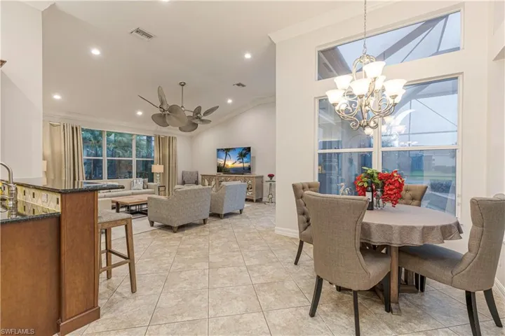 Tiled dining area featuring ceiling fan with notable chandelier, crown molding, and vaulted ceiling