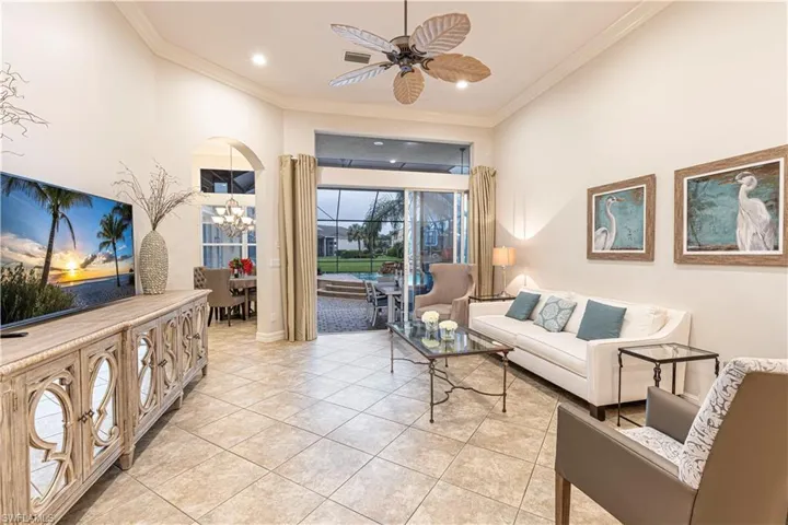 Tiled living room with ceiling fan with notable chandelier and crown molding