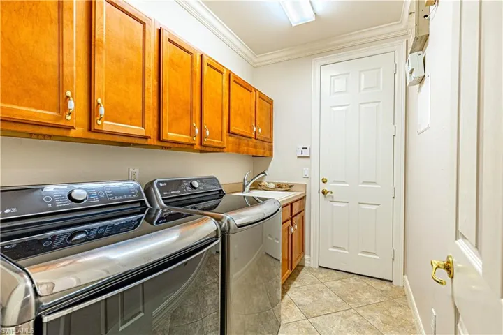 Washroom with cabinets, sink, washing machine and clothes dryer, light tile patterned floors, and crown molding