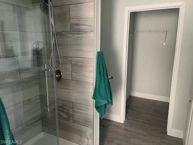 Full bath with a shower stall, dark wood-style floors, and a walk in closet