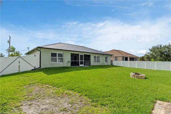 Expansive grassy backyard featuring a built-in stone fire pit, a full white vinyl privacy fence, and a screened-in patio area