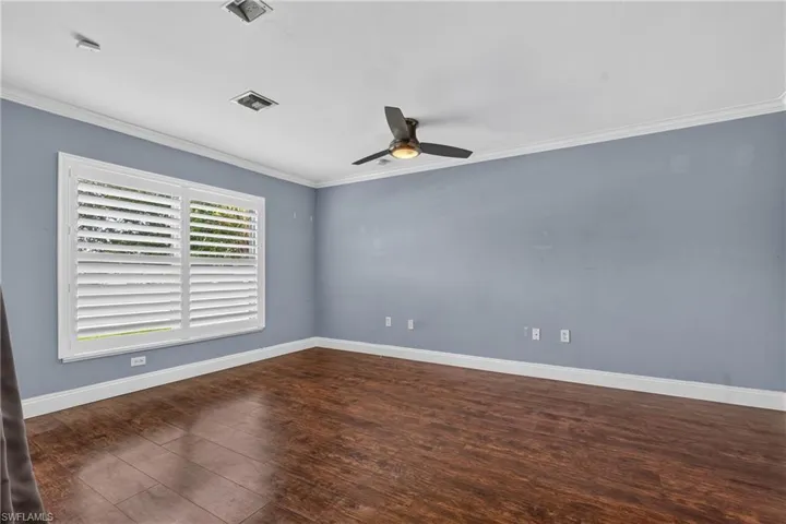 Spacious room featuring wood-finish flooring, white plantation shutters, crown molding, and a ceiling fan with integrated lighting