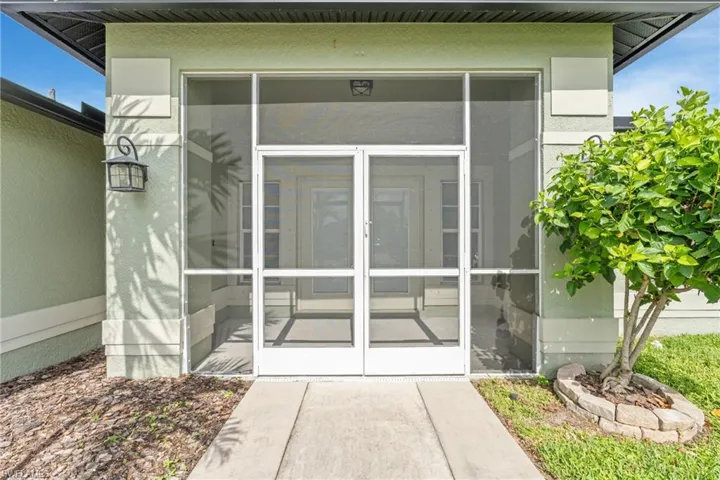 Screened entry porch with double doors, stucco exterior, concrete walkway, and a decorative outdoor lantern
