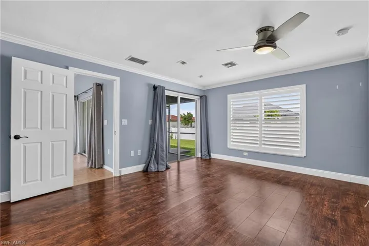 Spacious room featuring rich wood-finish flooring, a ceiling fan with integrated lighting, and crown molding