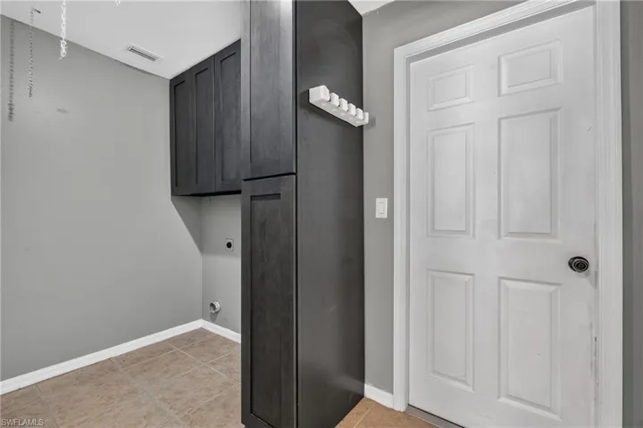 Utility space featuring dark wood-finish cabinetry, neutral wall paint, and square floor tiles