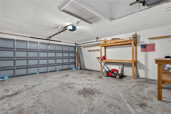 Spacious garage featuring a sectional garage door, concrete flooring, overhead lighting, and built-in wooden shelving for organization
