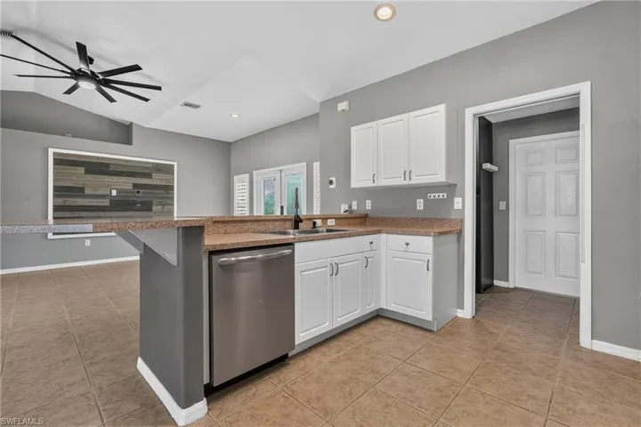 Kitchen featuring white cabinetry, a stainless steel dishwasher, and a breakfast bar with a speckled countertop