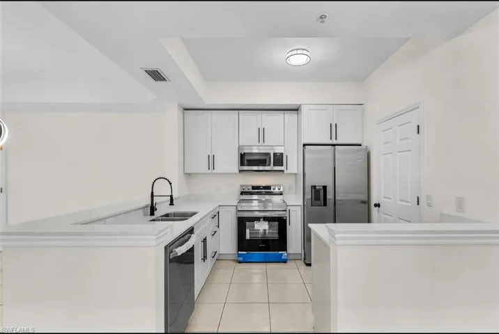 Kitchen with a peninsula, appliances with stainless steel finishes, light tile patterned flooring, white cabinets, and light stone counters