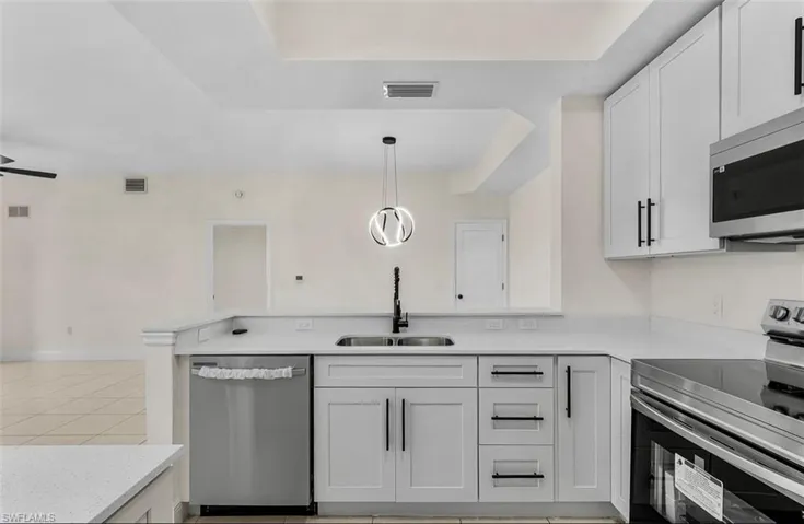 Kitchen with appliances with stainless steel finishes, white cabinets, light tile patterned floors, a peninsula, and hanging light fixtures