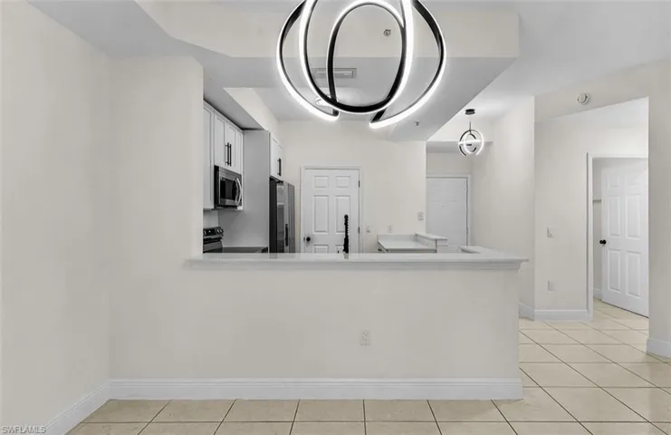 Kitchen featuring white cabinets, light tile patterned flooring, appliances with stainless steel finishes, a peninsula, and light stone countertops