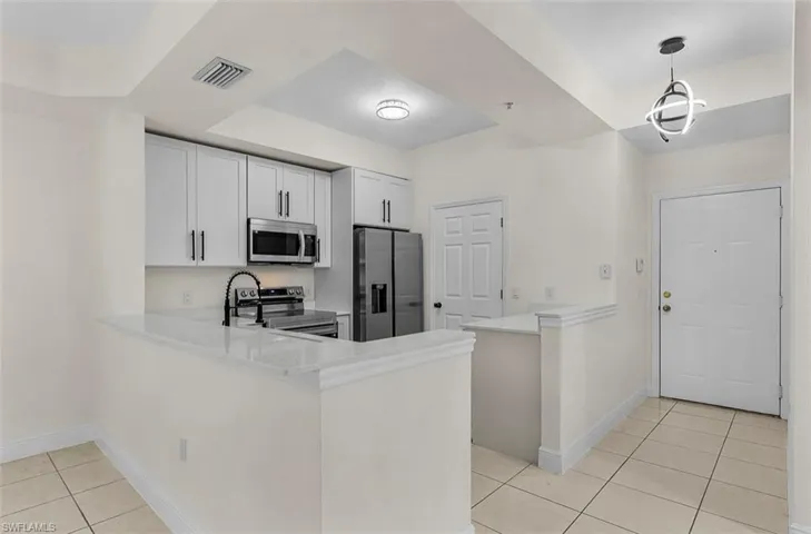 Kitchen with a peninsula, light tile patterned flooring, stainless steel appliances, and decorative light fixtures
