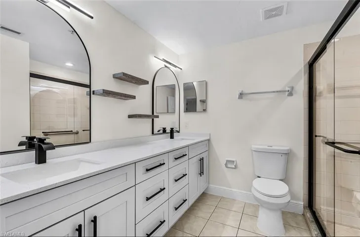 Full bath featuring double vanity, light tile patterned flooring, and a shower stall