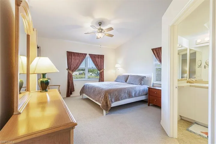 Bedroom featuring a ceiling fan, light carpet, ensuite bathroom, and lofted ceiling