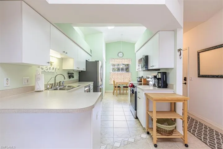 Kitchen featuring appliances with stainless steel finishes, white cabinets, vaulted ceiling, decorative light fixtures, and light countertops