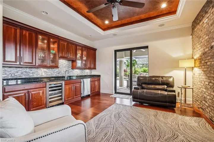 Indoor wet bar with wood cabinets, a raised ceiling, ornamental molding, dark wood finished floors, and wine cooler, refrigerator and recessed lighting