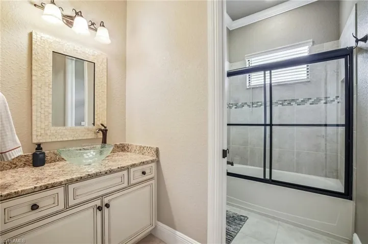 Bathroom featuring a textured wall, vanity, combined bath / shower with glass door, light tile patterned flooring, and crown molding