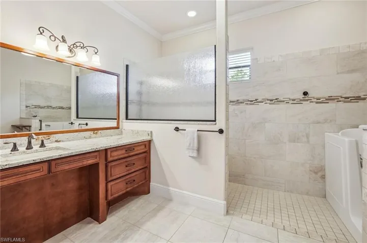 Full bath featuring vanity, walk in shower, light tile patterned floors, crown molding, wheelchair accessible