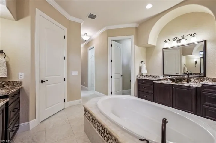 Bathroom featuring dual vanities, ornamental molding, light tile patterned flooring, and soaking tub