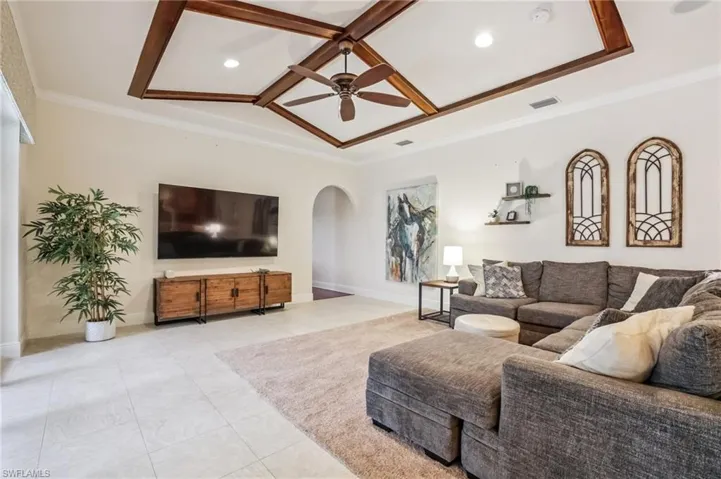 Living area with arched walkways, crown molding, ceiling fan, tile patterned floors, and coffered ceiling