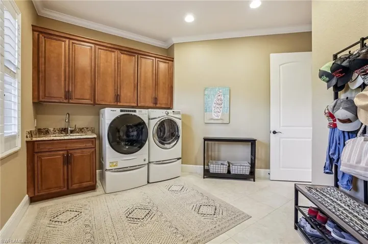 Laundry area featuring ornamental molding, stainless sink, washing machine and clothes dryer, cabinet space, light tile patterned flooring, and recessed lighting