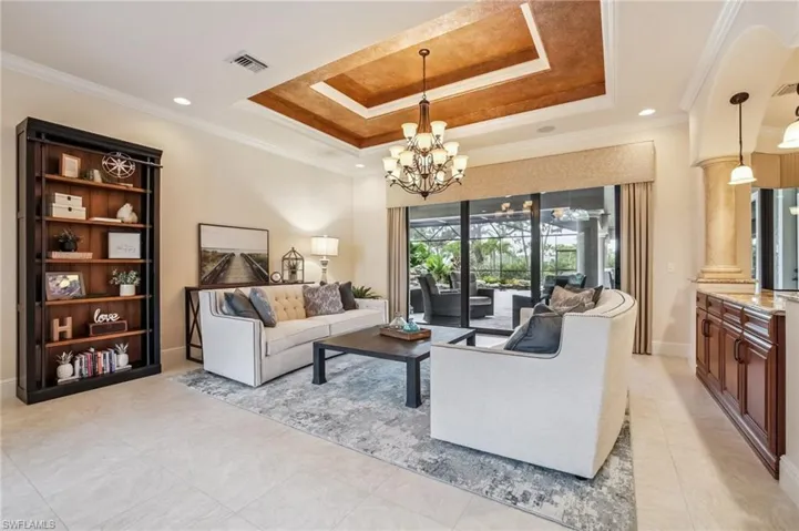 Living room with crown molding, a raised ceiling, recessed lighting, a chandelier, and light tile patterned floors