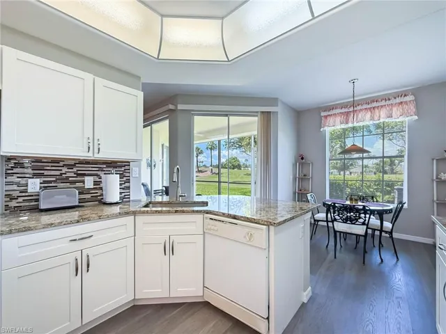 Kitchen featuring dishwasher, dark wood-style flooring, white cabinetry, a peninsula, and light stone countertops