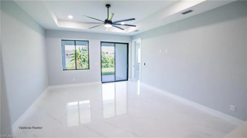 Empty room featuring light marble finish floors, a raised ceiling, a ceiling fan, and recessed lighting