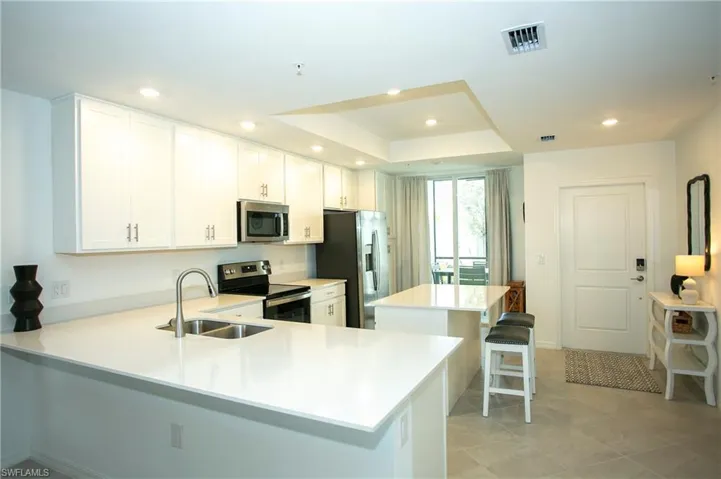Kitchen featuring a breakfast bar area, appliances with stainless steel finishes, white cabinets, a kitchen island, and a tray ceiling