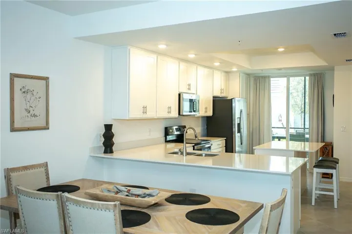 Kitchen featuring a peninsula, recessed lighting, white cabinetry, light stone counters, and appliances with stainless steel finishes