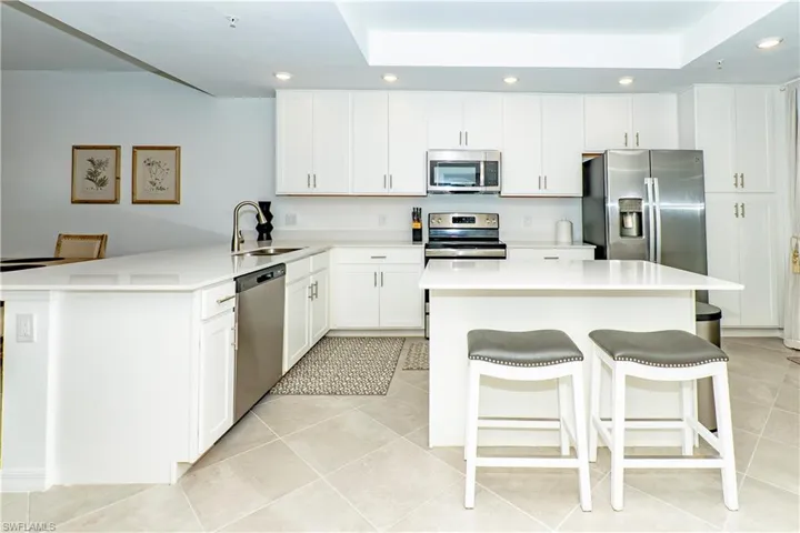 Kitchen featuring stainless steel appliances, recessed lighting, a tray ceiling, a peninsula, and white cabinets