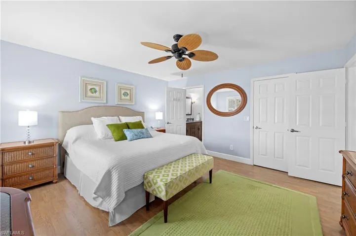 Large primary bedroom with ensuite bathroom, light wood finished floors, and ceiling fan
