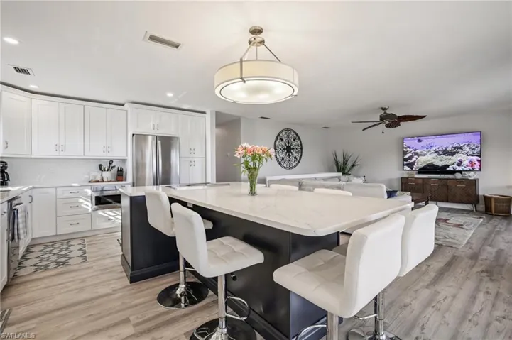 Kitchen with a breakfast bar, pendant lighting, a center island, light stone counters, and white cabinetry