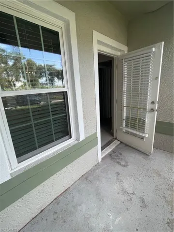 Exterior patio area featuring textured stucco siding, a white-framed window with integrated blinds, and a matching full-light door with integrated blinds