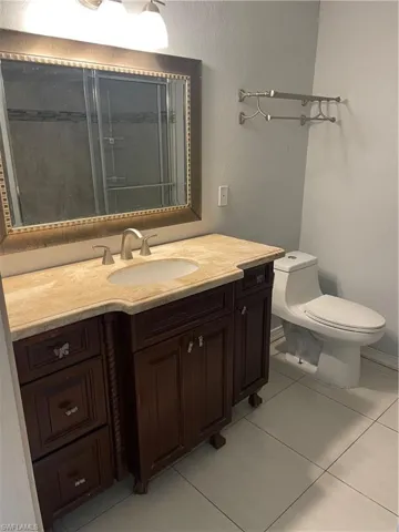 Bathroom featuring a dark wood-finish vanity with an integrated sink and light-toned countertop, a framed mirror, an overhead vanity light fixture, and ceramic tile flooring