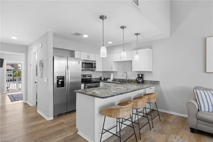 Kitchen featuring appliances with stainless steel finishes, a peninsula, a kitchen breakfast bar, white cabinetry, and light wood-style floors