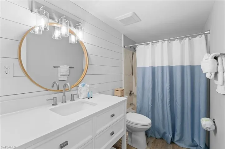 Bathroom featuring vanity, light wood-style floors, shower / bath combo, and wood walls