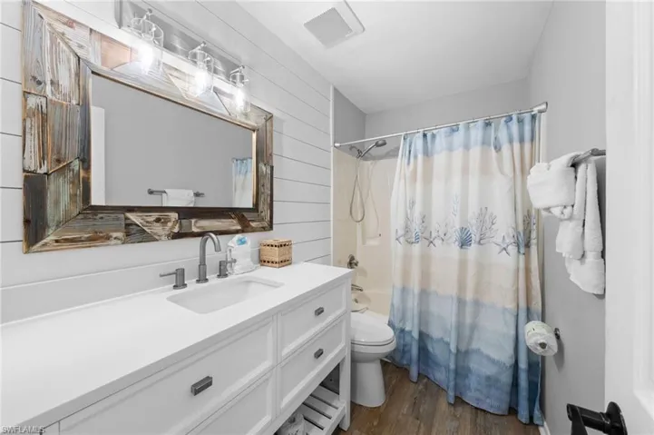 Full bath with shower / bathtub combination with curtain, dark wood-type flooring, vanity, and wooden walls