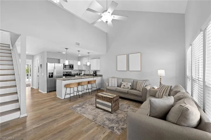 Living room featuring stairs, high vaulted ceiling, light wood-style flooring, and a ceiling fan