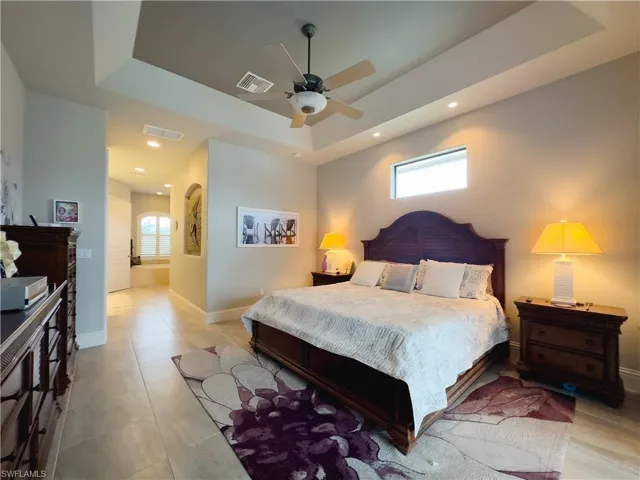 Primary Bedroom featuring ceiling fan, light tile floors, and a tray ceiling
